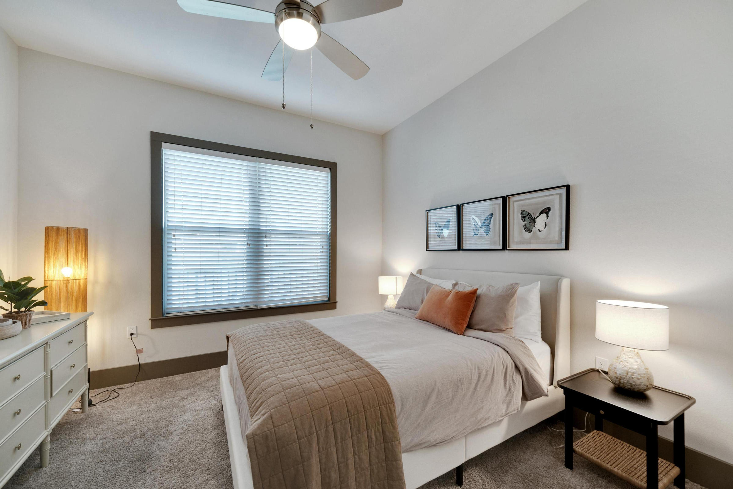 Modern bedroom with a bed, nightstands, lamps, dresser, and butterfly artwork above the headboard.