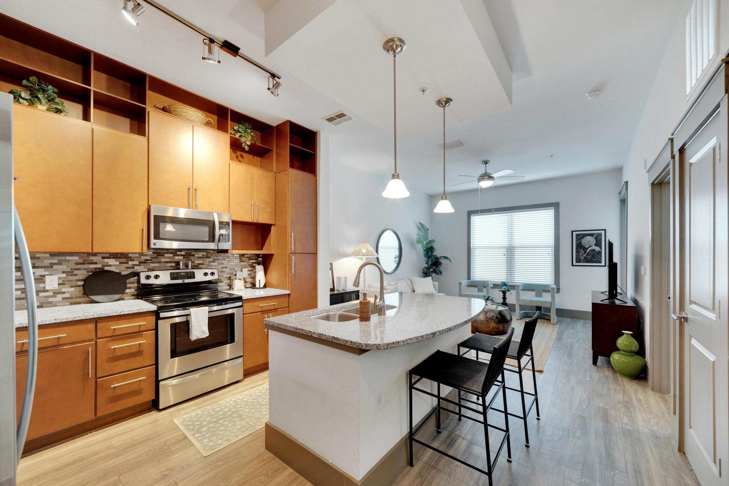 Modern kitchen with wood cabinets, stainless steel appliances, and island with barstools, open to living area.