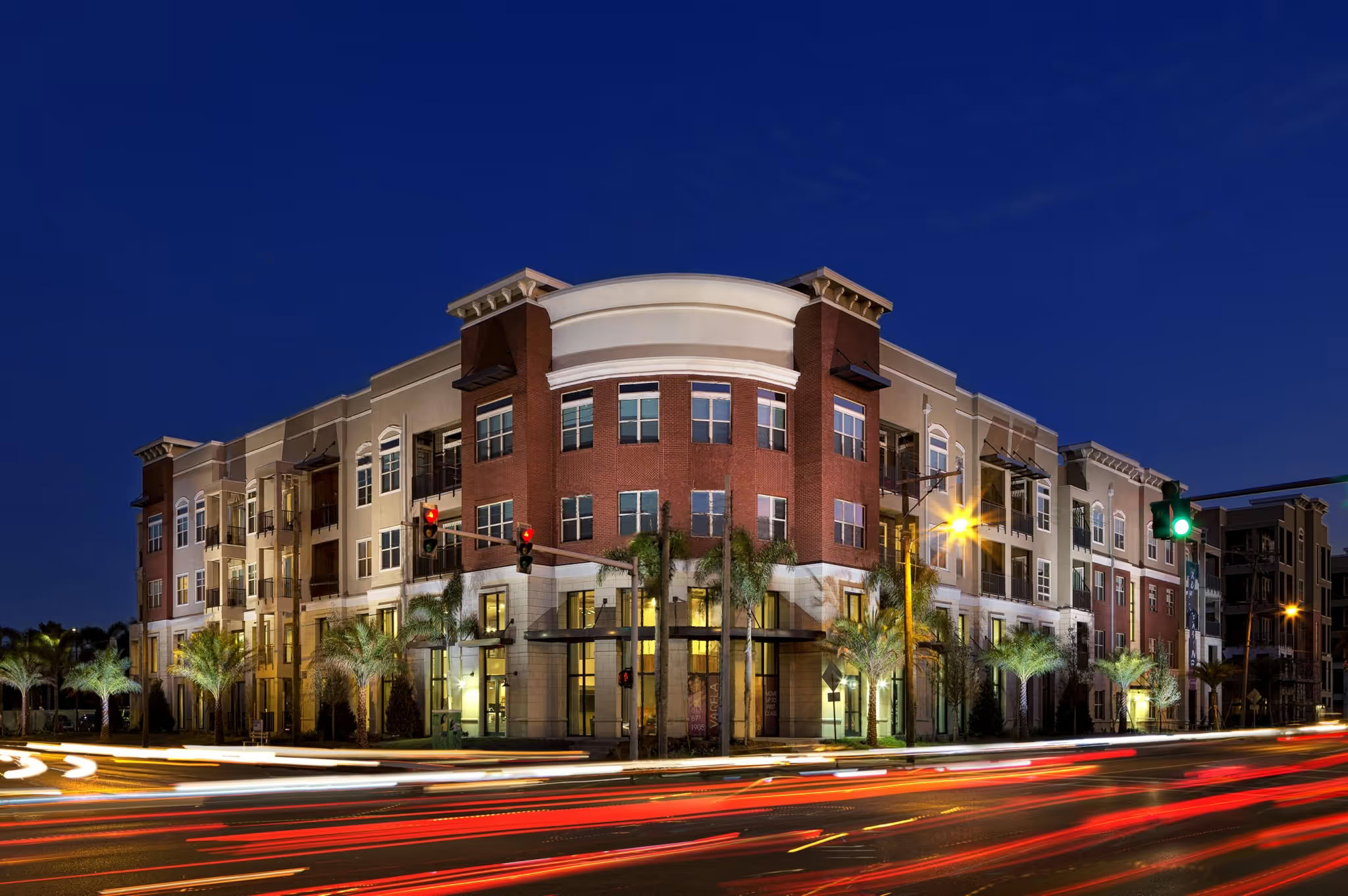 A modern apartment building at night in Tampa FL, with palm trees and light trails—enjoy walkable living at Varela Westshore.
