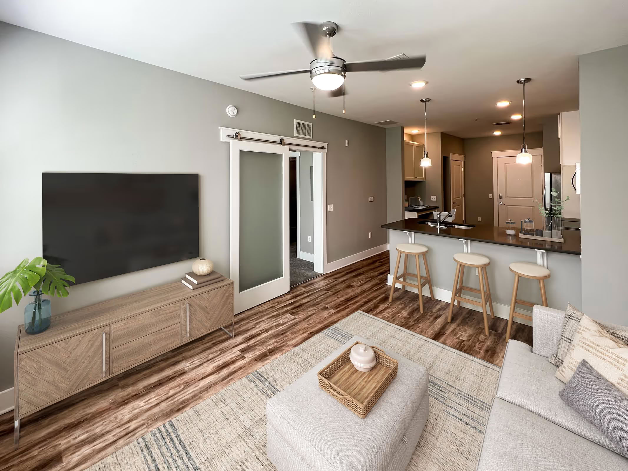 Modern living room at Varela Westshore in Tampa FL featuring walkable living, TV, cozy sofa, and kitchen island under pendant lights.