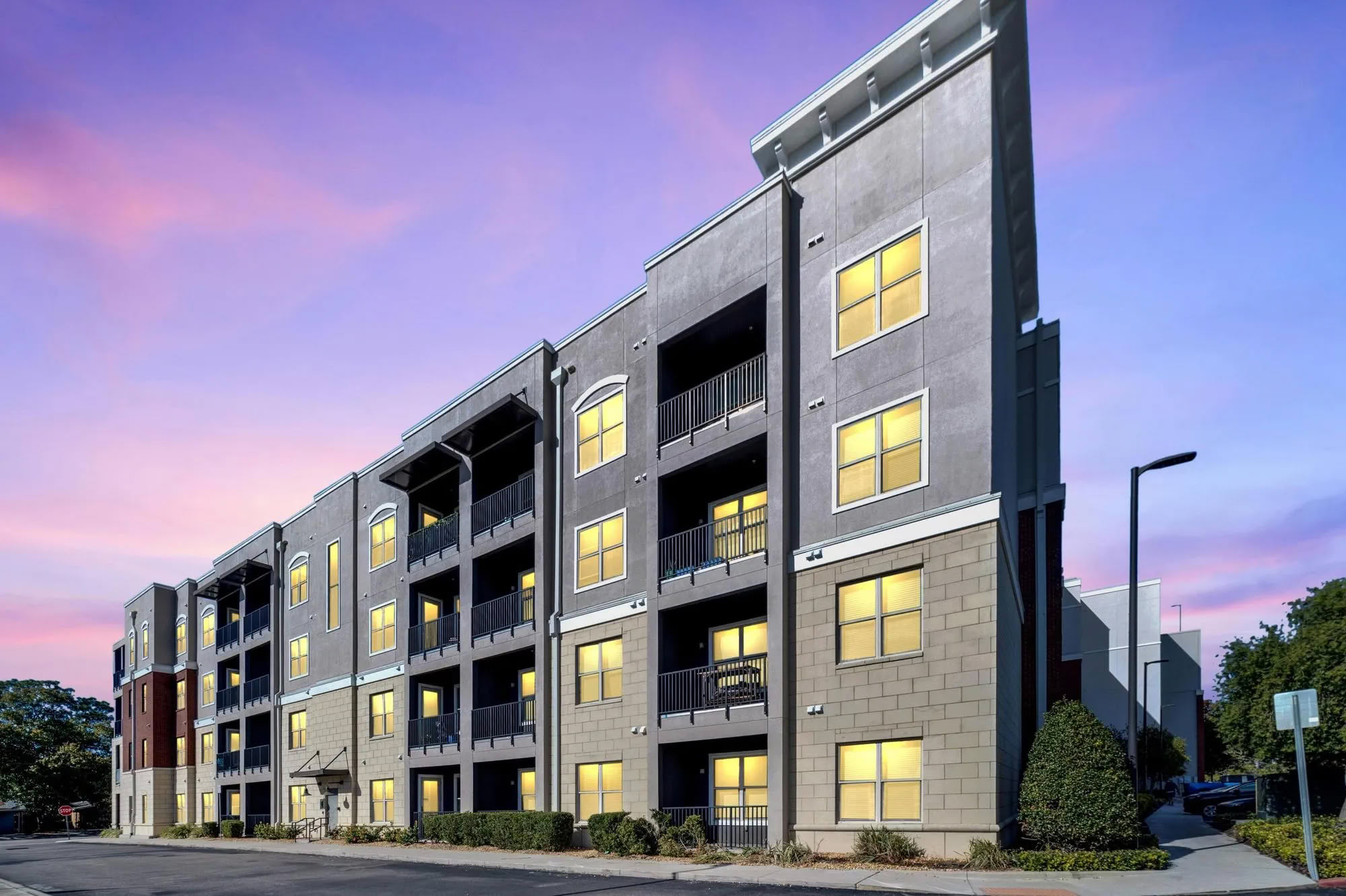 Modern four-story Varela Westshore apartment building with lit windows at dusk, set against a colorful Tampa FL sunset sky.
