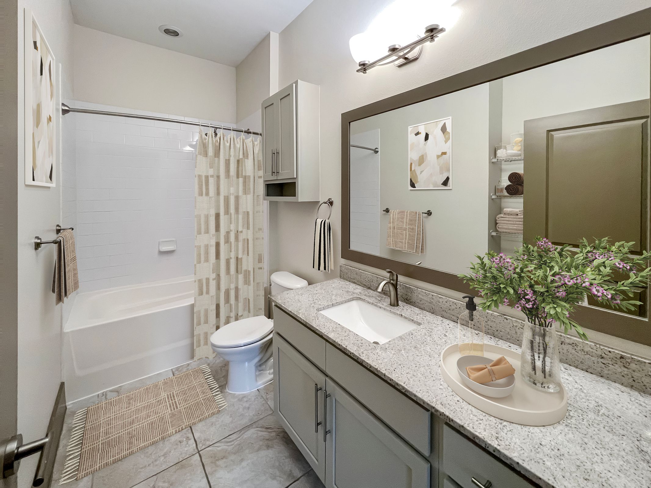 Modern bathroom with granite countertop, large mirror, bathtub with shower curtain, and vase of flowers on the sink.