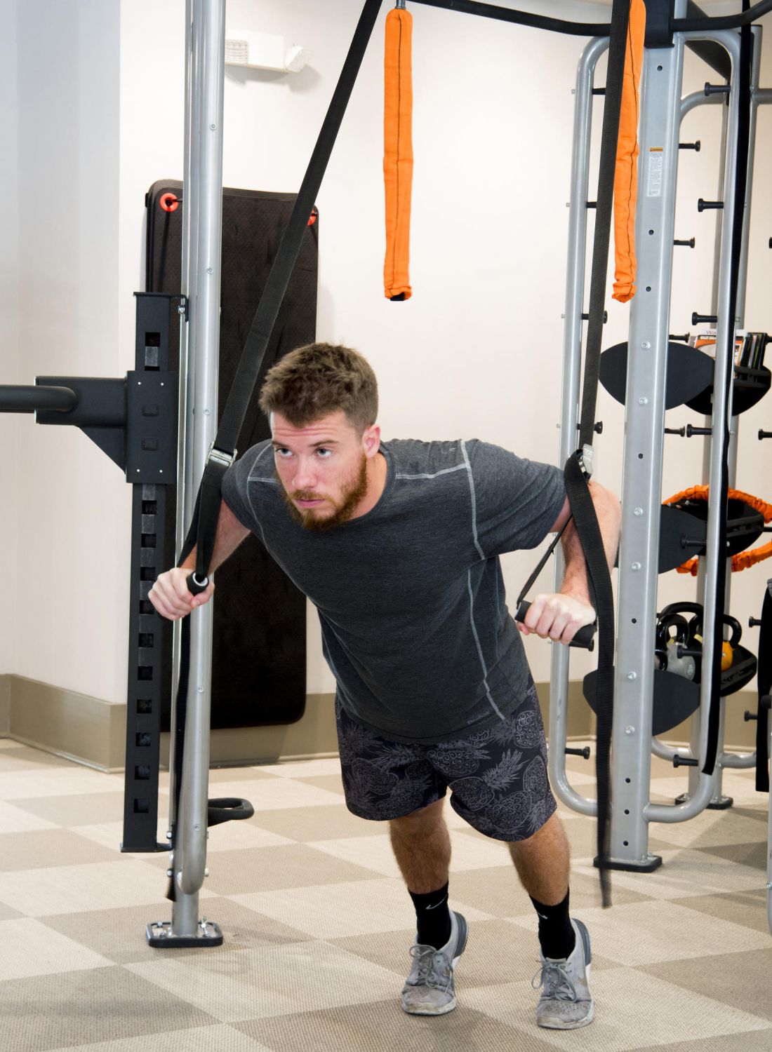 Man exercising with suspension straps in a gym, leaning forward while holding the straps.