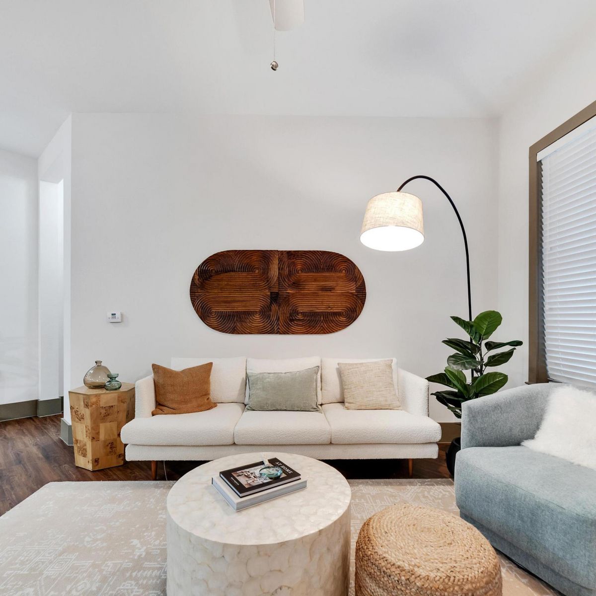 Modern living room with a white sofa, gray chair, plants, and wall art, featuring neutral, cozy decor.