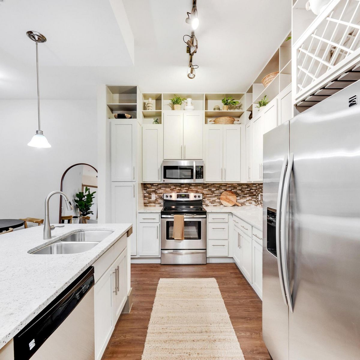 Modern kitchen with stainless steel appliances, white cabinets, island sink, and dining area in the background.