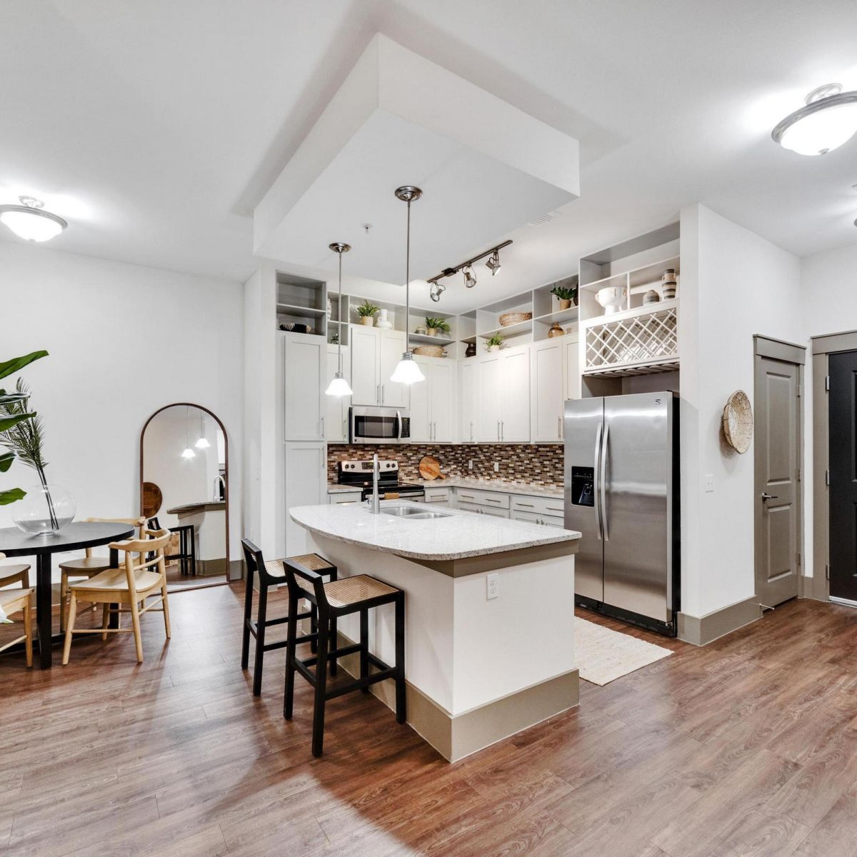 Modern kitchen and dining area with island, stainless steel appliances, wood floors, and bright lighting.