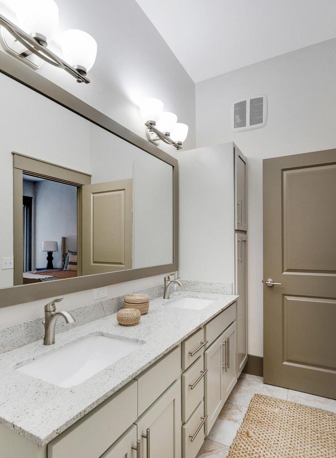 Modern bathroom with dual sinks, large mirror, beige cabinets, and tan towels hanging on the wall.