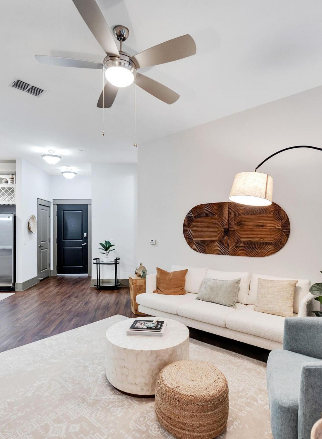 Modern living room with neutral colors, a white sofa, round ottomans, and open kitchen in the background.