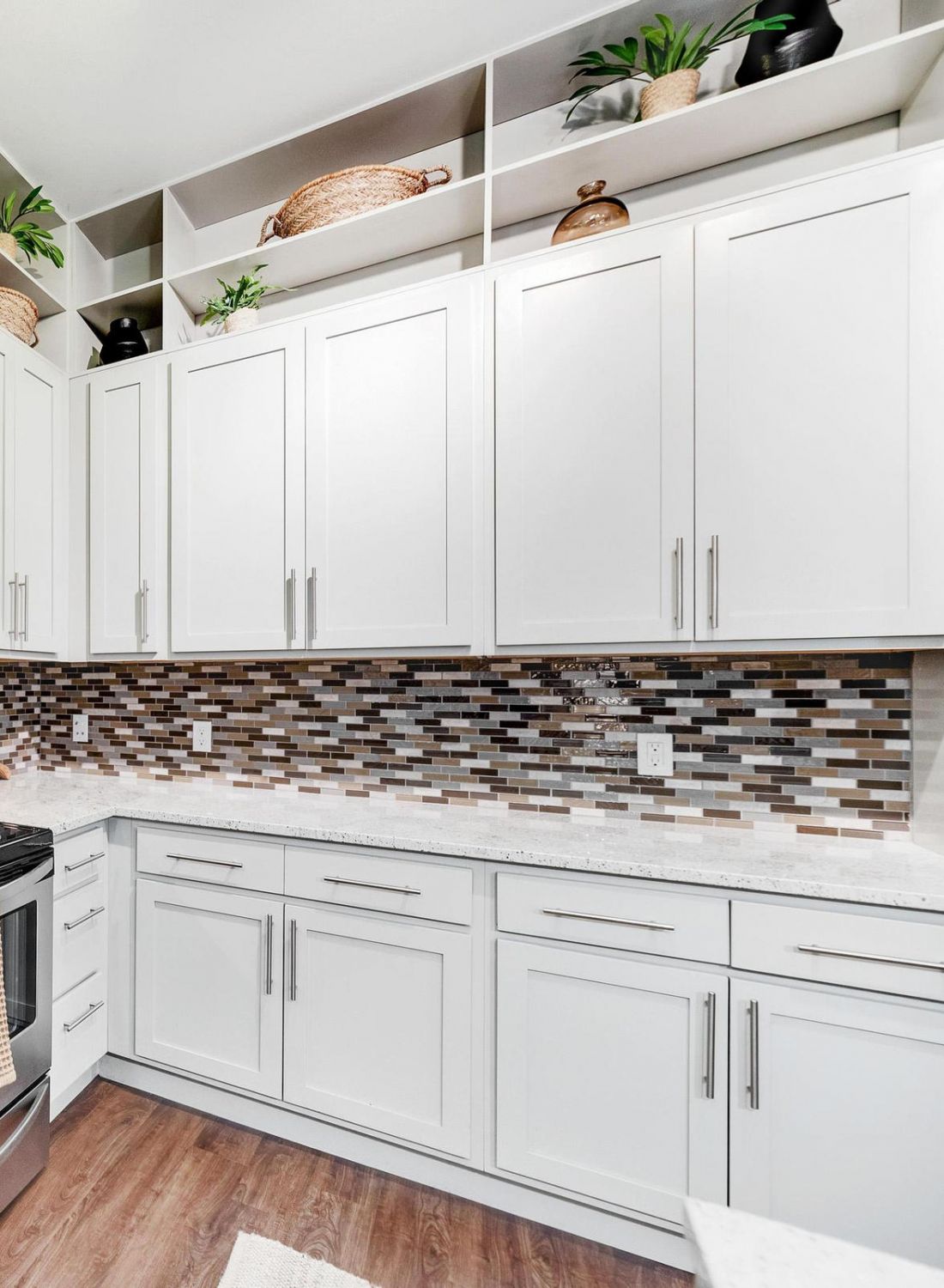Modern kitchen with white cabinets, stainless steel appliances, mosaic backsplash, and wood flooring.