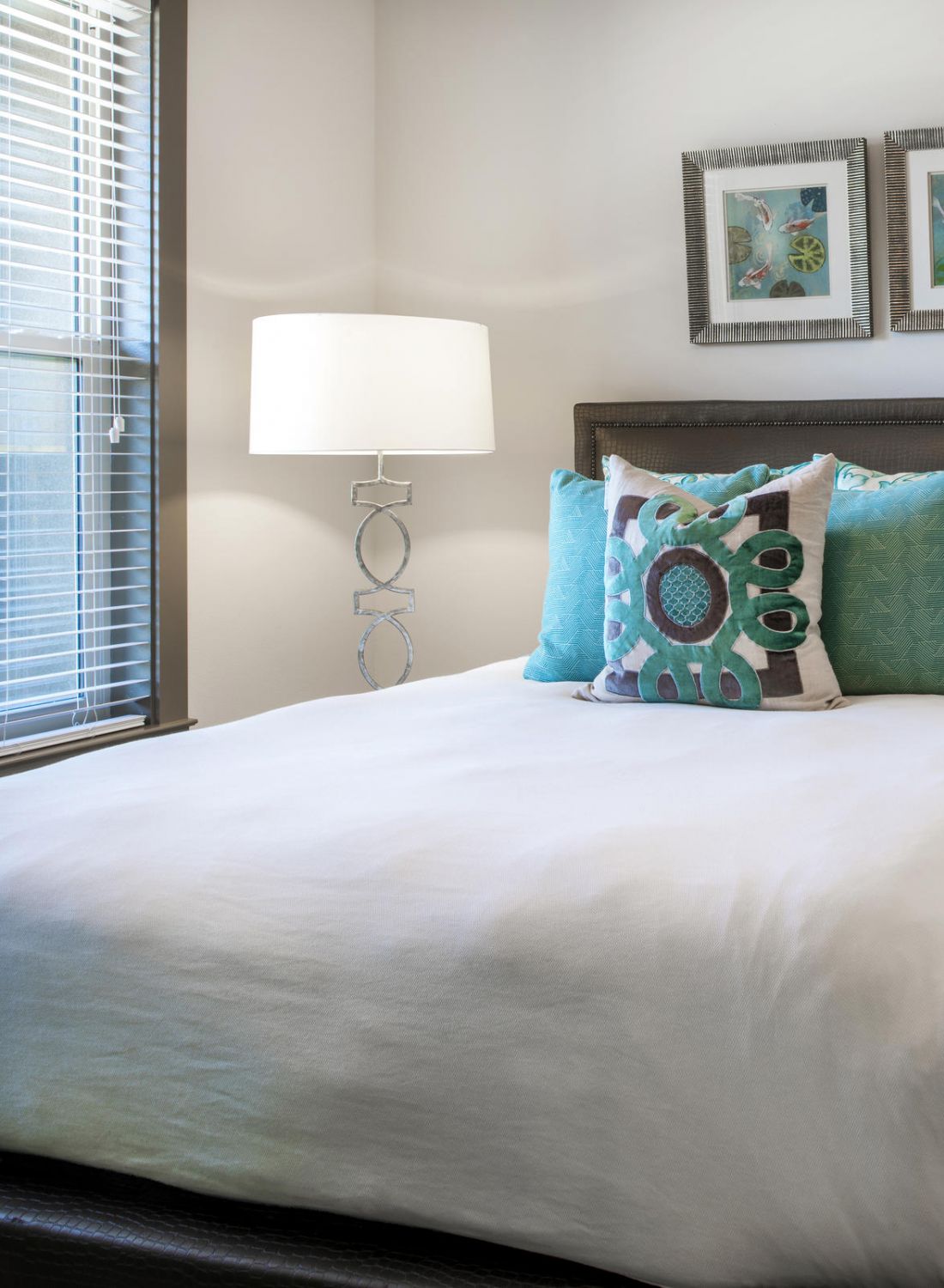 Modern bedroom with a neatly made bed, green nightstand, lamps, and two framed pictures on the wall.