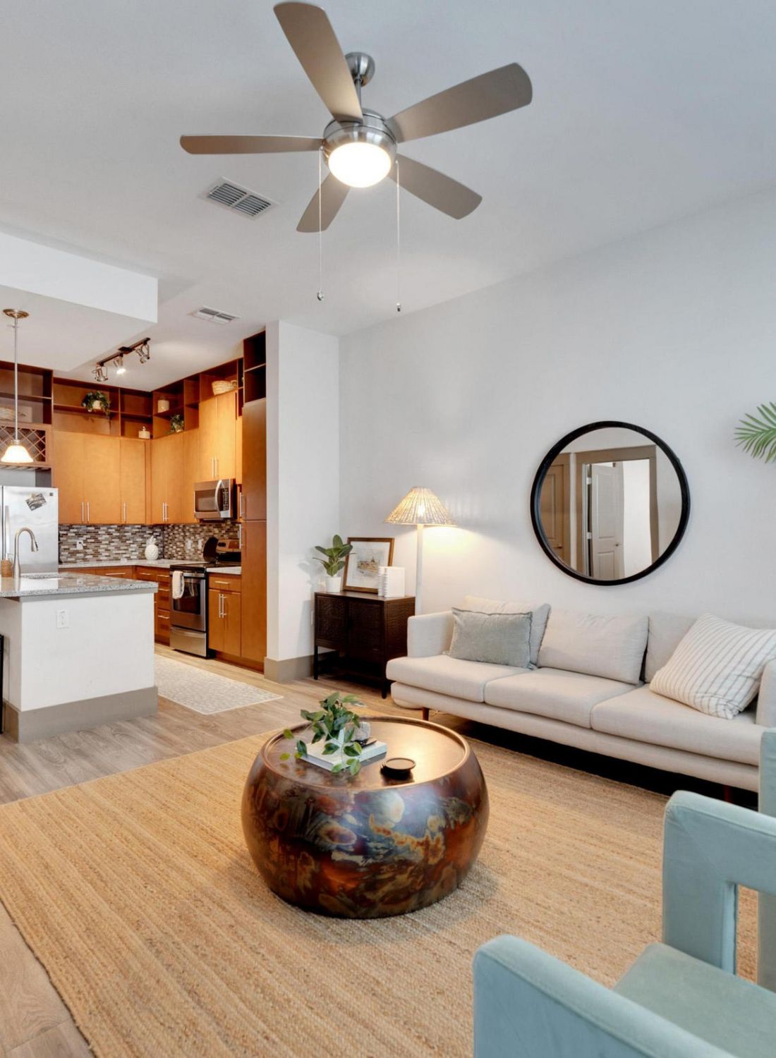 Modern living room with sofa, round coffee table, plant, and open kitchen in the background.