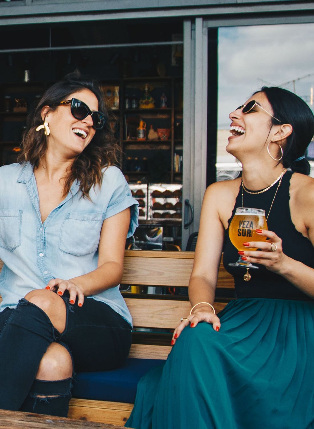 Two girlfriends sitting outside and having a beer at a local bar 