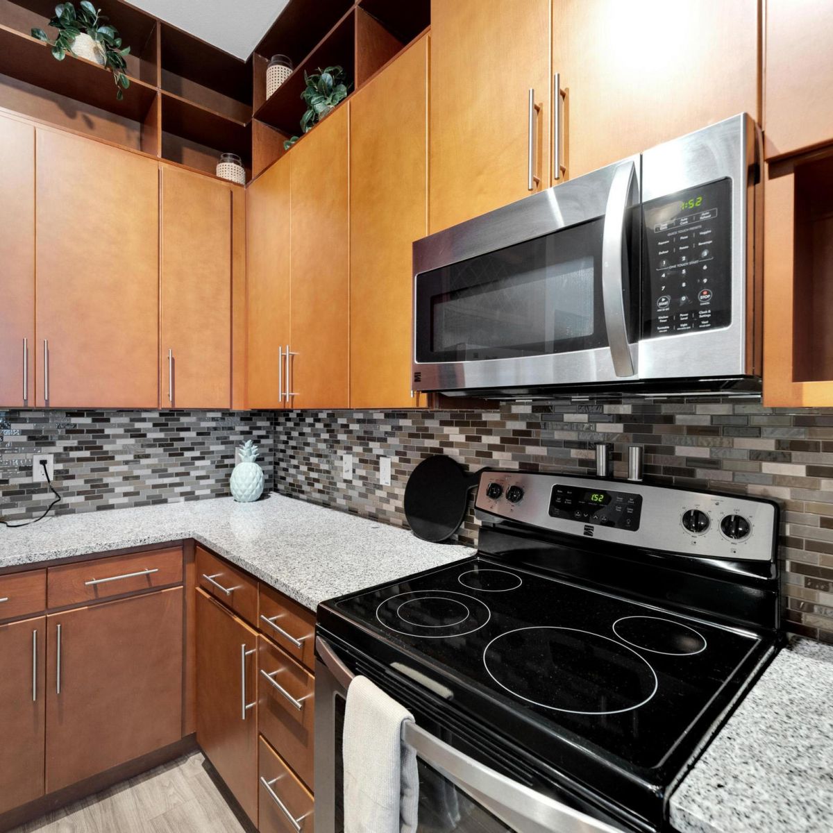 Modern kitchen with wooden cabinets, stainless steel appliances, and a gray mosaic tile backsplash.